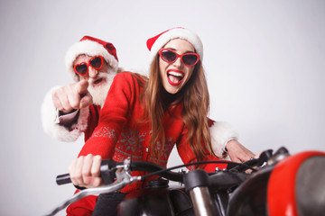 Happy young mrs. Claus wearing Santa hat, red sweater and sunglasses sitting with Santa Claus on a motorcycle, New Year, Christmas, holidays, souvenirs, gifts, shopping, discounts, shops, Snow Maiden