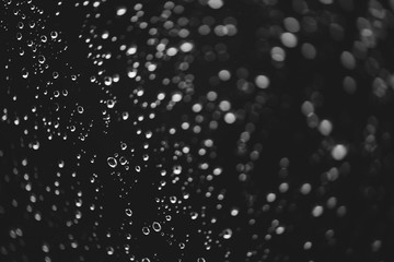 Naklejka na ściany i meble Dirty window glass with drops of rain. Atmospheric monochrome dark background with raindrops in bokeh. Droplets and stains close up. Detailed transparent texture in macro. Copy space. Rainy weather.