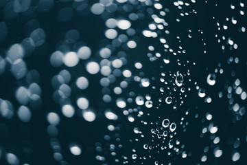 Dirty window glass with drops of rain. Atmospheric blue background with raindrops in bokeh. Droplets and stains close up. Detailed transparent texture in macro with copy space. Rainy weather.