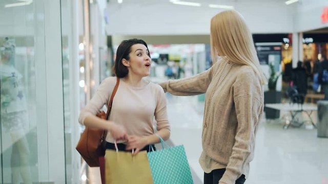 Pretty girls are meeting in shopping mall, showing purchases in paper bags and discussing prices and clothing. Shopaholism, retail and youth lifestyle concept.