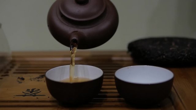 Man pour tea from an earthenware teapot into bowls. Chinese tea ceremony