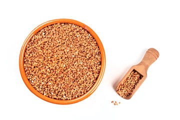 A photo of raw buckwheat in an earthenware bowl with a scoop, shot from above on a white background with copy space