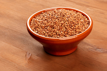 A photo of raw buckwheat in an earthenware bowl on a dark rustic wooden background with copy space