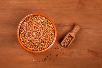 A photo of uncooked buckwheat in an earthenware bowl with a scoop, shot from above on a dark rustic wooden background with copy space