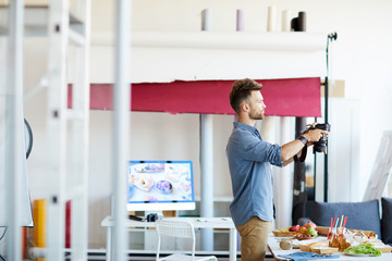 Side view portrait of young photographer taking pictures of food in studio, copy space
