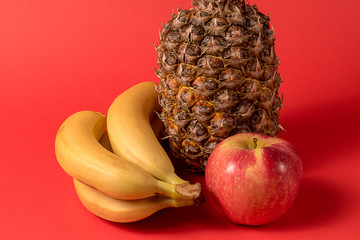 fruit - pineapple fruit, apple and banana over red background.