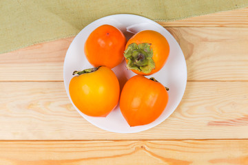 Persimmon fruits on white dish on wooden rustic table