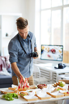 Waist up portrait of smiling photographer taking pictures of party table with food