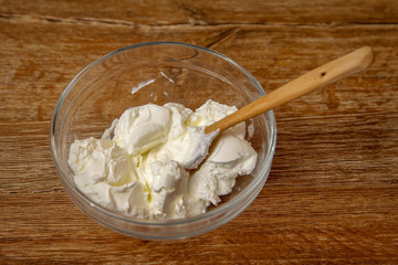 Sour cream in the glass bowl with wooden spoon on rustic wooden table