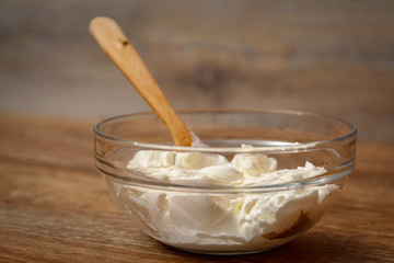 Sour cream in the glass bowl with wooden spoon on rustic wooden table