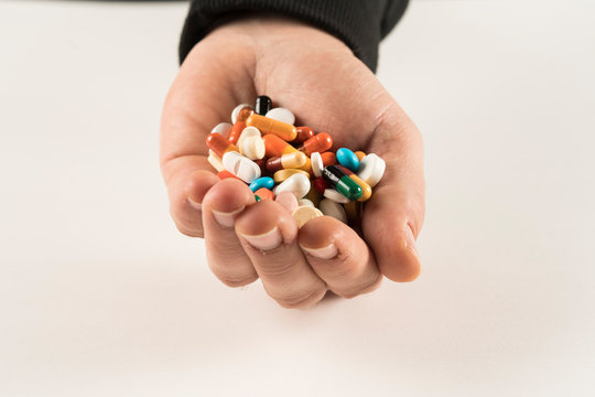 Male hand holding high number of  pills on white blackground. High resolution image for pharmaceutical industry.