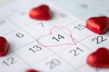 valentines day and holidays concept - close up of calendar sheet with marked 14th february date and red heart shaped chocolate candies