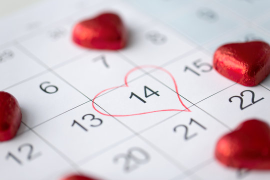 valentines day and holidays concept - close up of calendar sheet with marked 14th february date and red heart shaped chocolate candies - Powered by Adobe