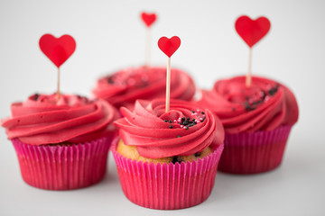 valentines day, food, baking and pastry concept - close up of cupcakes or muffins with red buttercream frosting and heart cocktail sticks