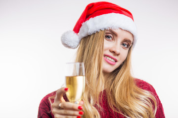 Close-up portrait of an attractive smiling young blonde woman in a red Santa hat and a knitted sweater holding a champagne glass on white background. Christmas, new year and celebration concept