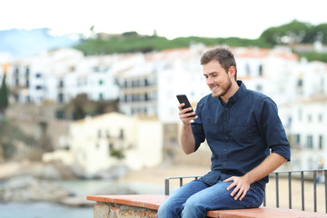 Fototapeta na wymiar Happy man on a ledge using a smart phone