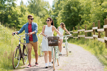 people, leisure and lifestyle concept - happy young friends with fixed gear bicycles on road in summer