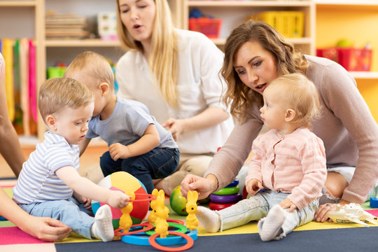 Group of babies toddlers playing with colorful educational toys and mothers in nursery room