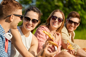 friendship, leisure and food concept - group of smiling friends eating pizza at picnic in summer...