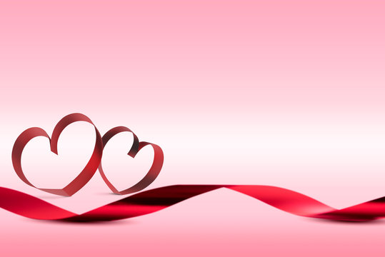 Red ribbons with ribbons shaped as hearts over pink background