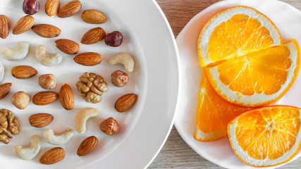Assorted Nuts, Orange Slices On White Plates On Wooden Table. Healthy Organic Snack, Breakfast, Food Ingredients. Flat Lay Top-Down Composition.