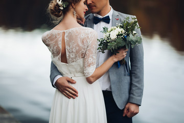 Back view of husband embracing his beautiful elegant wife in lace wedding dress with lovely bouquet...