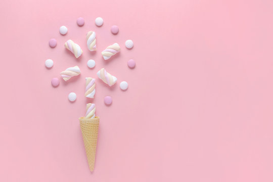 candy, marshmallow and ice cream waffle cone on pink background, concept image