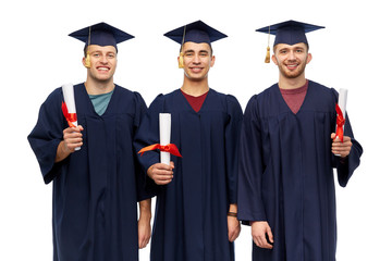 education, graduation and people concept - group of happy male graduate students in mortar boards and bachelor gowns with diplomas over white background