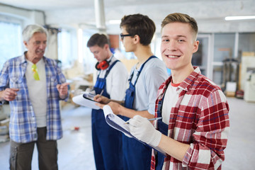 Content excited handsome young carpentry worker in gloves standing in row of interns at...