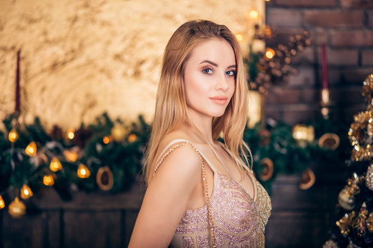 Portrait of luxurious blonde woman in Golden evening dress on Christmas tree and candles background. Sexy beautiful girl smiles and looks down. Holidays, celebration and people
