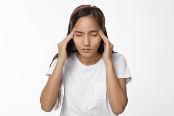People, health and sickness concept. Brunette Asian student girl in white t-shirt closing eyes and squeezing her head, having bad headache, suffering from stress while preparing to important exams