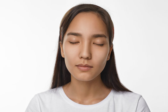 Peace, calmness, harmony and meditation concept. Beautiful young Asian woman with loose black hair having peaceful serene facial expression while meditating in studio, keeping her eyes closed