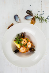 An overhead photo of a seafood risotto on teal textures, with a fork and a spoon, a glass of white wine, and a place for text