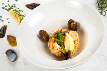 An overhead photo of a seafood risotto on teal textures, with a fork and a spoon, a glass of white wine, and a place for text