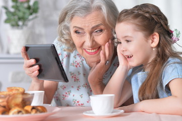 Cute little girl with her grandmother looking at tablet 