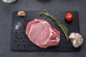 Raw bone steak with spices on a black stone. Uncooked meat. Top view.