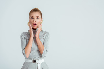 surprised woman touching face with hands and looking at camera isolated on grey