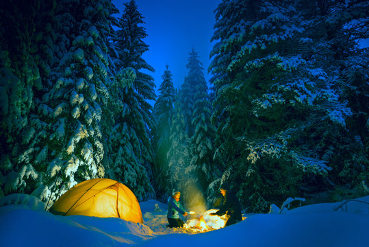 couple camping with campfire and tent outdoors in winter