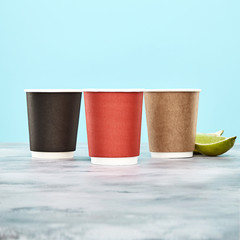 multicolored coffee cup on blue background. disposable paper dishes. Brown, red, black cups. Copy space for logo, text or brand
