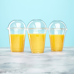 Fresh orange juice in plastic glasses on blue background. Free copy space for text, logo or brand
