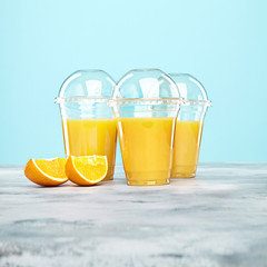 Fresh orange juice in plastic glasses on blue background. Free copy space for text, logo or brand