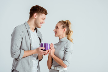 handsome man giving present to beautiful woman isolated on grey