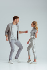 beautiful couple in grey clothing looking at each other and dancing isolated on grey