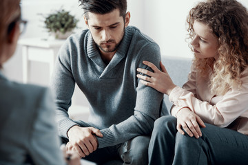 Supportive beautiful wife touching husband's arm during psychotherapy session for married couples with problems