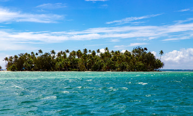 Landscape of little island with palm trees, seen from the water surface in the lagoon, Pacific ocean, French Polynesia