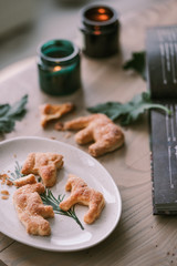 Homemade shaped cookies on a wooden table next to candles, green leaves and a cookbook. Crumbs are scattered at ease on the table. The concept of Christmas atmosphere and comfort.