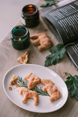Homemade shaped cookies on a wooden table next to candles, green leaves and a cookbook. Crumbs are scattered at ease on the table. The concept of Christmas atmosphere and comfort.
