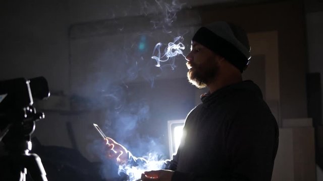 A man with a beard smokes and looks into the phone