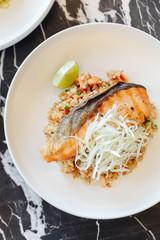 Garlic fried rice with grilled salmon served with chili bean sauce on black marble top table.