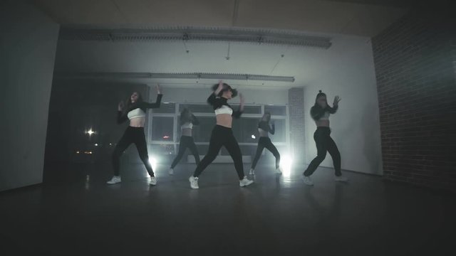 Girls enjoying funky hip hop moves in dark studio with smoke and lighting. Group of young hip-hop dancers performing on the stage. Happy dancing women.